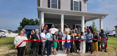 Leaders and community members standing in front of the new transitional house to cut the ribbon.