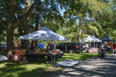 Multiple white tents with vendors at the Worcester County Fair grounds. The sun shines through green trees.