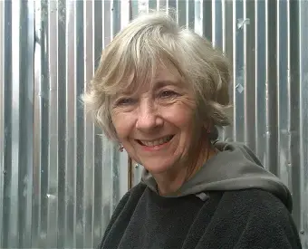 Woman with short gray hair, wearing a black and gray hooded jacket standing in front of a silver aluminum wall.