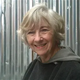 Woman with short gray hair, wearing a black and gray hooded jacket standing in front of a silver aluminum wall.