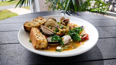 Clams, spinach, and baguette plated on a white plate sitting on a black composite round table 