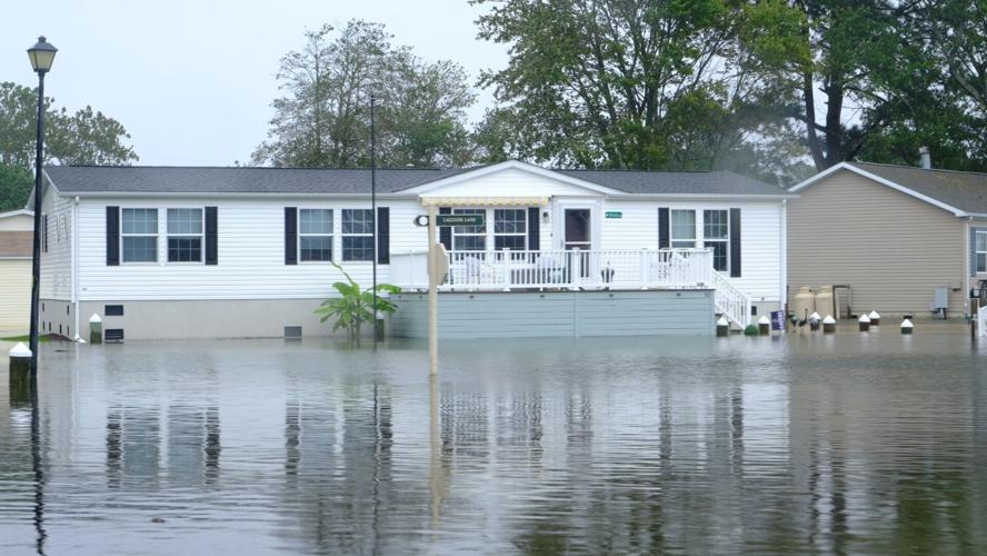 A white manufactured home with a front porch surrounded by water.