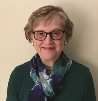 Woman with light brown hair, wearing dark frame glasses, earrings, black sweater with a scarf, with a beige color background