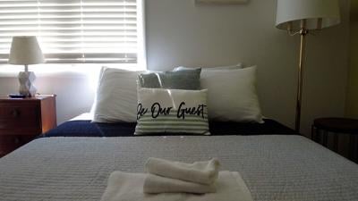 Bed inside of a short-term rental with pillow reading, "Be Our Guest"