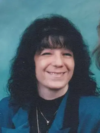 woman, black shoulder length hair., wearing black mock top covered with teal vest with aqua back ground