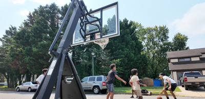 Children and youth playing basketball with a portable basketball hoop on a Dover neighborhood street.