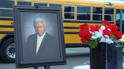A framed picture of Bill Handy next to a vase of flowers, with a yellow school bus in the background.