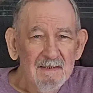 man with Short salt & pepper hair, mustache, and goatee. wearing a purple t-shirt 
