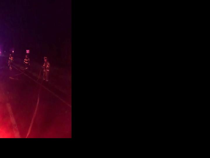 Firefighters stand in a roadway while responding to a crash scene off US 113 with a sedan fully engulfed by flames.