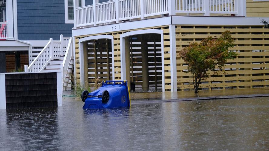 A blue garbage can lays on its side in front of a garage. The yard is covered with water.
