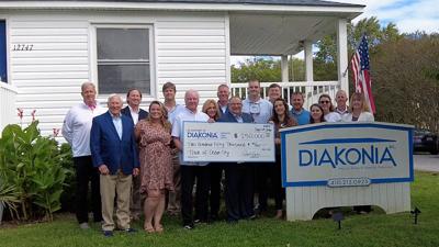 Ocean City town leaders and Diakonia officials gathered in front of Diakonia Food Pantry. Ken Argot is holding a check presented by Mayor Rick Meehan for $250,000. Everyone in photo is smiling next to 'Diakonia" sign. 
