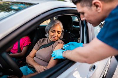 A senior woman being vaccinated inside of her car. 