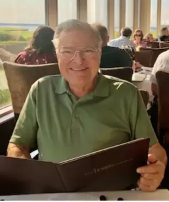 Man with gray hair, wearing glasses and olive green polo shirt in restaurant holding a menu.