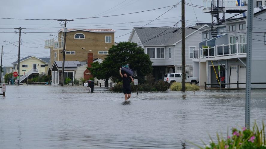 A man carries a suitcase through water up to his knees.