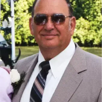 man with bald head, wearing sunglasses, white dress shirt, gray suit and trees in the background