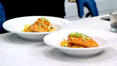 Two plates of glazed salmon topped with green onions, plated in white bowls