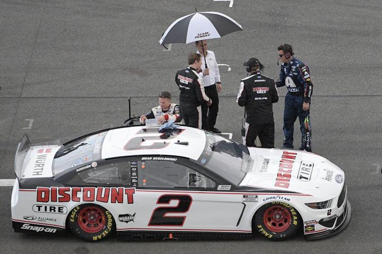 Brad Keselowski stands under an umbrella on pit road as rain forces a red flag during the NASCAR Daytona 500
