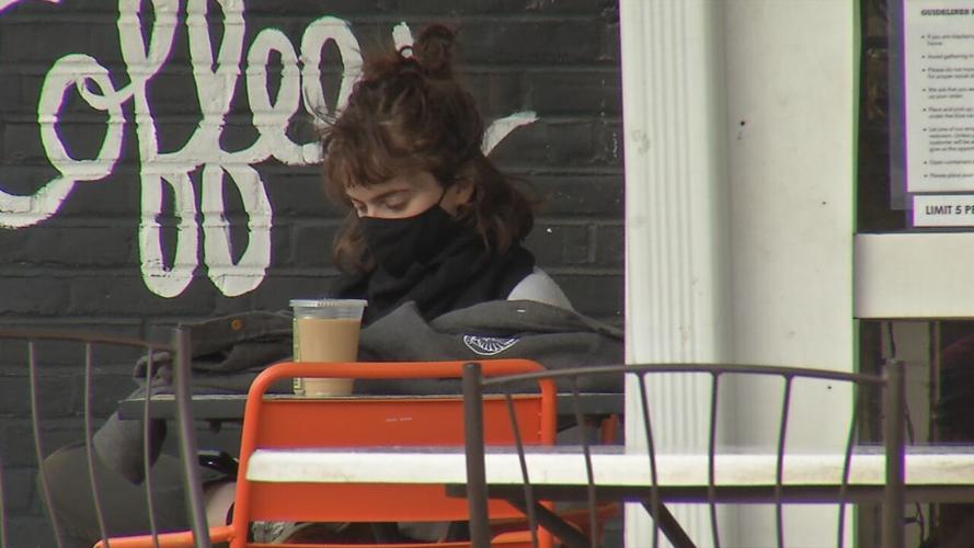 Customer gets coffee to-go and sits outside Safai Coffee while indoor seating is closed