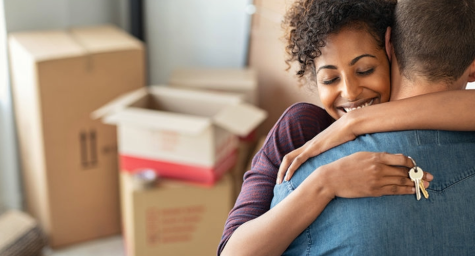 Couple hugging while holding keys to their new home with moving boxes behind them,