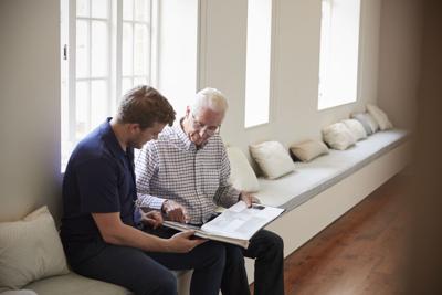 Senior man sitting looking at photo album  with male nurse