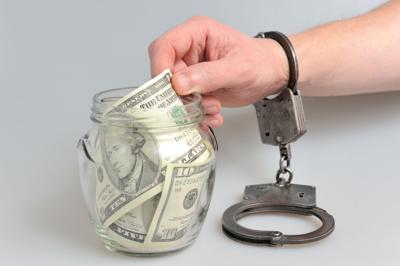Handcuffed hand reaching into money jar