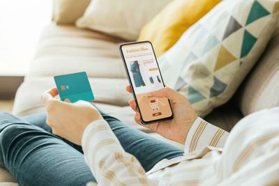 Stock photo of a woman buying a dress online with the phone and a credit card from the sofa at home