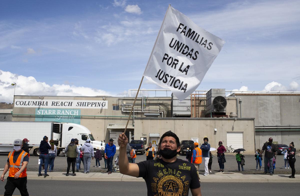 Alex Palma, a striking Matson Fruit employee, waves a Familias Unidas por la Jusicia flag in front of Columbia Reach Pack on Thursday, May 14, 2020, in Yakima, Wash. Palma was part of a caravan of hundreds of workers from Columbia Reach Pack, Jack Frost, Matson, Monson, Hansen, and Allan Bros. that traveled between the protests happening in front of the warehouses. Evan Abell/Yakima Herald Republic 